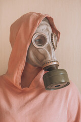 Portrait of a woman in a gas mask,  head turned to the side. Woman in a pink sweater with a hood...