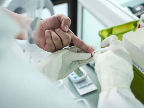 Overhead view a finger prick blood test. A patient is tested for Covid-19 via rapid antibody test using a disposable blood lancet. Possible test for blood sugar level too.