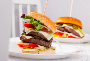 Two fresh tasty double burgers with cheese, lettuce salad, onion, tomatoes and marinated cucumbers