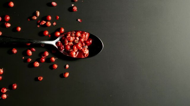TOP VIEW: Spoon with pink pepper seeds fall on a black table. Slow motion, Splash.