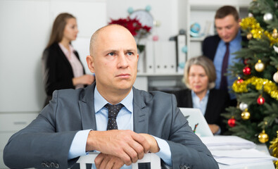 Upset businessman sitting in office with working colleagues behind