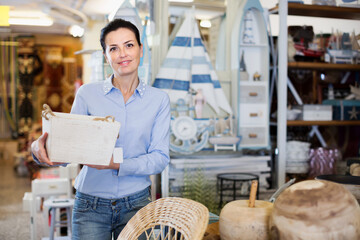 Smiling female holding items for her house in a modern home decor store..