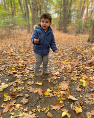 Photo of Moroccan toddler stand in middle of woods holding a small stick looking at camera during autumn