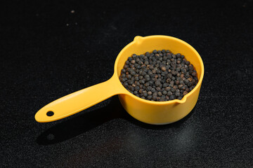 Black Pepper in yellow spice spoon on black background'