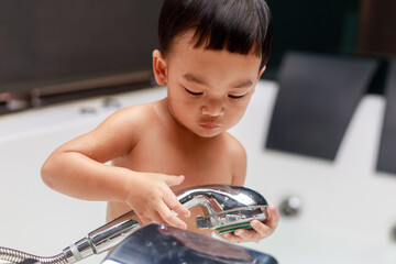 Adorable Asian kid boy (Toddler age 1-year-old) take a shower in the white bathtub by himself, Encourage Self-Help Skills at home