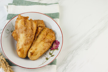 Pisang Goreng or Banana fritters, Indonesian traditional snack made from banana and flour, deep fried. Served on white plate, with a cup of tea. Isolated white background. Copy space for text. 