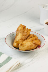 Pisang Goreng or Banana fritters, Indonesian traditional snack made from banana and flour, deep fried. Served on white plate, with a cup of tea. Isolated white background. Copy space for text. 