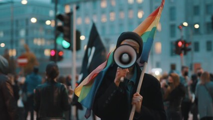 Woman with face mask speaking into the megaphone while holding rainbow flag. Demonstration against dicrimination . High quality 4k footage