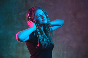 Young woman in headphones with dreadlocks with multicolored neon lighting on dark background. Stylish girl with headphones dancing in futuristic environment.