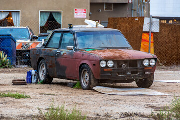 Rusty old classic Datsun sits in an empty dirt lot.