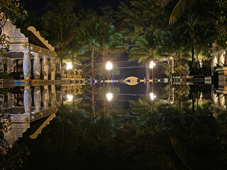 night view of palm trees in sparkling garlands reflected lights in the surface of the water