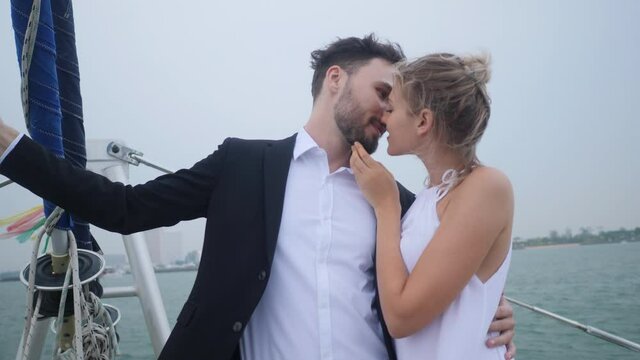 A couple celebrating their wedding on a yacht, wear a black suit and white dress.