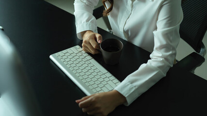 Female hand holding coffee mug on office desk with computer keyboard
