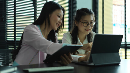 Two female consulting on their project, pointing on digital tablet screen