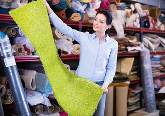 Cheerful satisfied smiling woman consumer shopping and holding carpet indoors