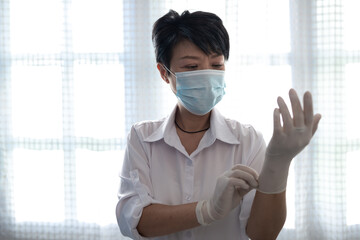 Senior Asian woman is wearing a protective face mask while wearing the surgery gloves during the Coronavirus Covid-19 crisis. Hygiene concept