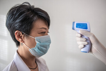 Hand holding infrared thermometer to measuring temperature on Asia woman with face mask with white background. Covid19 screening. And a new normal concept