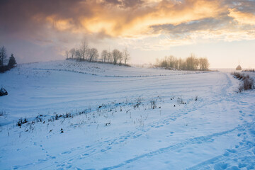 foggy countryside at dawn. beautiful rural landscape in wintertime. trees on snow covered hills beneath a glowing sky