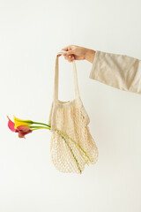 Woman holding a reusable net bag with pink calla lillies flower