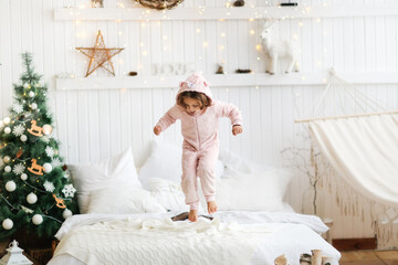 Fototapeta na wymiar cozy caucasian christmas child happily jumping on the bed in a light casual interior, home photos of children, concept new year and christmas,