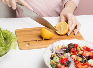 A woman halves a lemon on a cutting Board to add lemon juice to a Greek salad