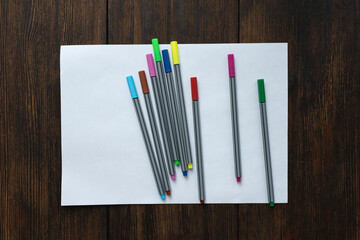 Blank, white sheet of paper with colored markers on dark wooden background