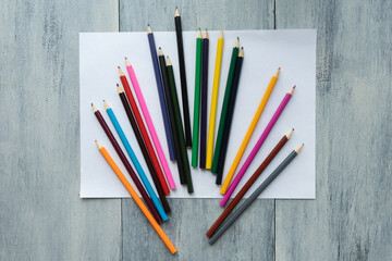 Blank, white sheet of paper with colored pencils on white wooden background