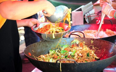 Chinese chicken lo mein cooked in a wok outdoors.