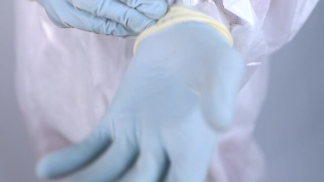 Nurse in protective PPE suit putting on gloves