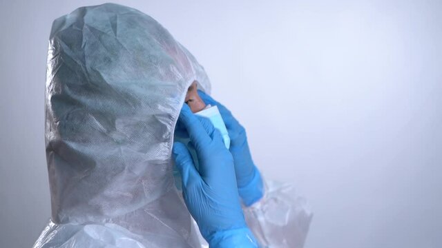 Nurse in profile putting on the hood of a PPE protective suit