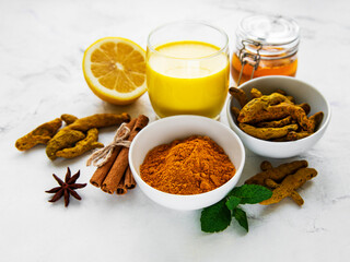 Yellow turmeric latte drink. Golden milk with cinnamon, turmeric, ginger  and honey over white marble background.