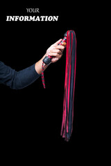 Leather whip in male hand isolated on black background. Strict black and red whip in man's hand....