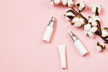 White skin care cosmetic bottles on pink background with cotton flowers. Bio beauty products packaging design. Advertising cosmetics product. Flat lay, top view. Concept beauty. Copy space.