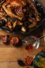 Close-up view of dish with baked turkey and potato near autumn harvest and glass with the remains of red wine on wooden background. Concept of festive dinner.