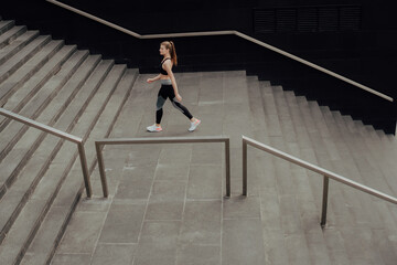 A young girl in a tracksuit runs up the stairs, in a business center.