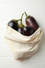 Cotton bag with fresh eggplants on wooden background