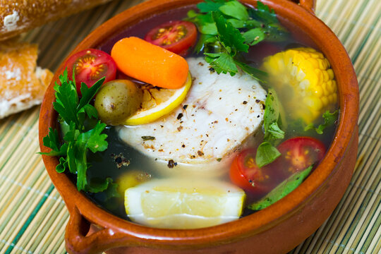 Fisher soup from merluccius. Recipe: boil broth from fish head, add potatoes, carrots, shallots, corn, fish fillets or steak 200 g, season with salt, pepper. Then cook in oven at 200 deg for 40min