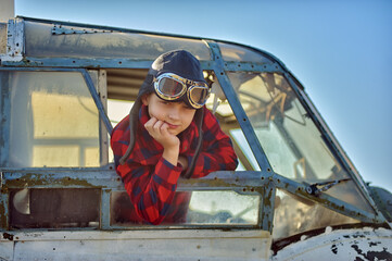 Portrait of a happy boy in a flying retro helmet in the cockpit of an old plane