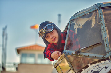 Portrait of a happy boy in a flying retro helmet in the cockpit of an old plane