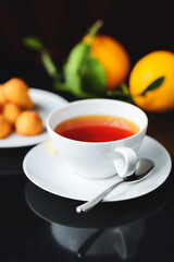 White glass cup with black, red tea with lemon on a dark glass table.
