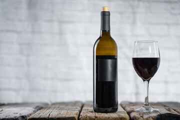 Elegant wine bottle and glass with red wine stands on the rustic wooden table on gray background. Space for text. Advertisement concept.