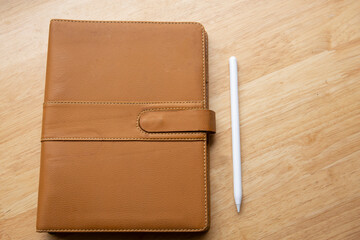 top view of brown leather notebook with pen on wooden table