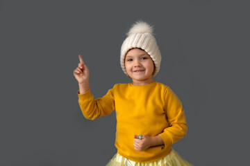 A funny Caucasian girl in a white knitted and yellow sweater shows on the background on a gray background, the concept of children's emotions and antics,