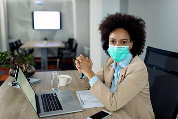Black businesswoman with protective face mask working on laptop in the office.