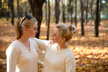 Fototapeta premium Mother and daughter in the park. Autumn and yellow leaves. Young mother and her toddler girl have fun.