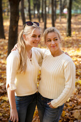 Mother and daughter in the park. Autumn and yellow leaves. Young mother and her toddler girl have fun.