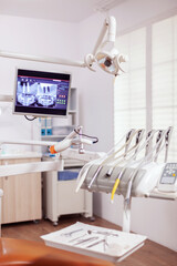Close-up view of dental tools and professional chair at dentist. Stomatology cabinet with nobody in it and orange equipment for oral treatment.