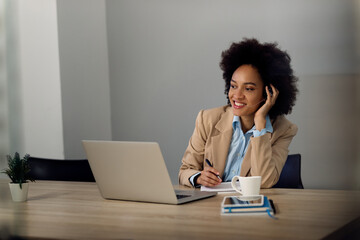 Happy black businesswoman taking notes during conference call over laptop in the office.
