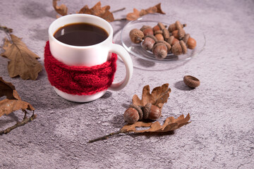 Acorn coffee Cup with acorns on a glass plate, oak leaves, concrete background. Cup in a knitted scarf. A substitute for coffee.