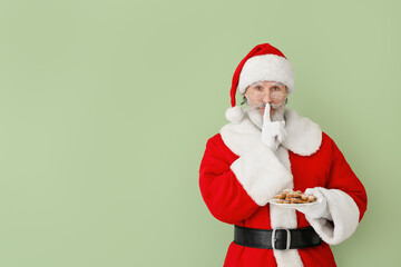 Fototapeta na wymiar Santa Claus with tasty gingerbread cookies showing silence gesture on color background